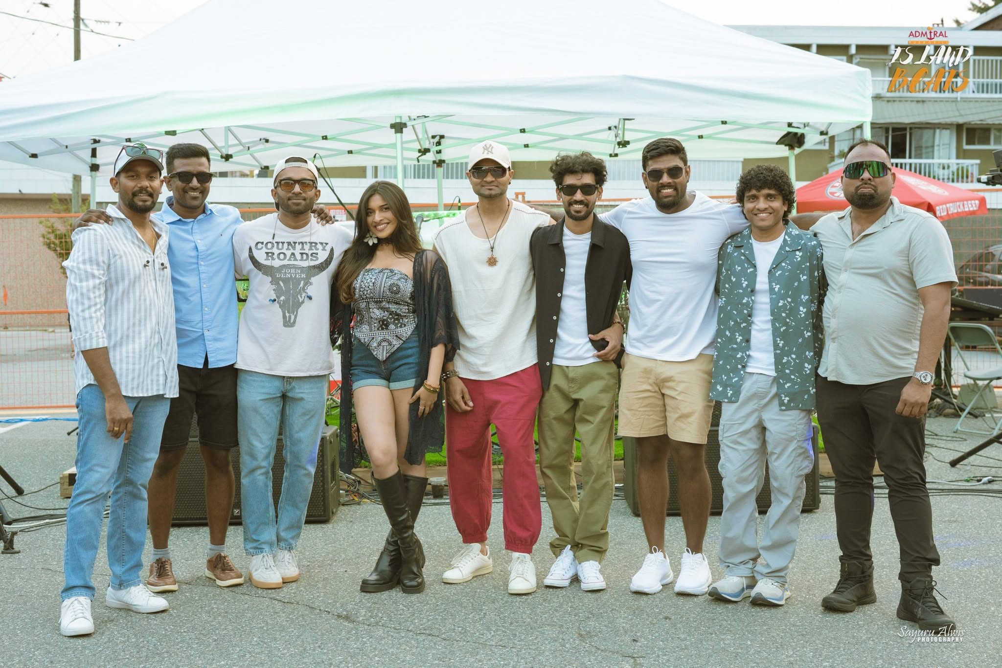 The nine members of Legacy Music standing together in front of their outdoor festival stage